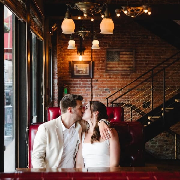 A couple kisses in a red booth at Revolution House, with brick walls and an American flag.
