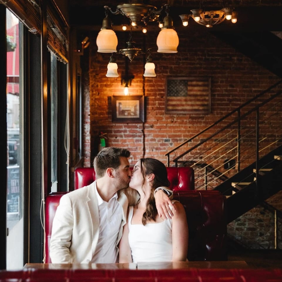 A couple kisses in a red booth at Revolution House, with brick walls and an American flag.