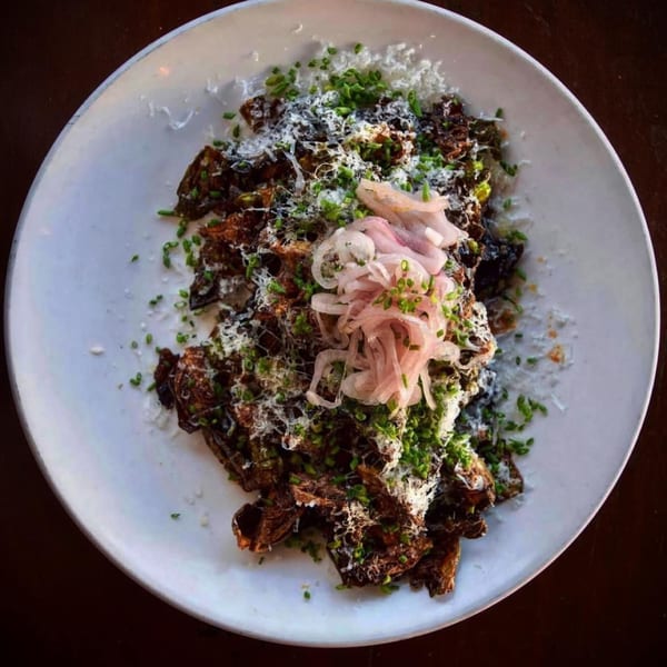 Crispy Brussels sprouts with pickled onions, grated cheese, and chives on a white plate.