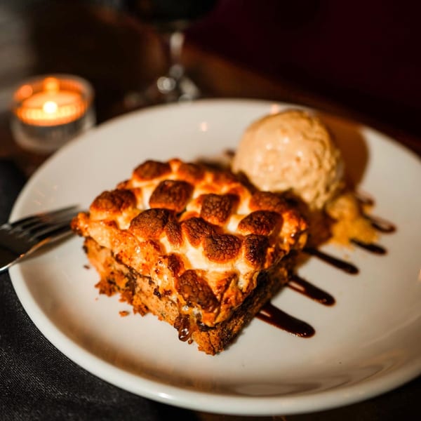 A s'mores dessert with toasted marshmallows and ice cream on a white plate, next to a candle.