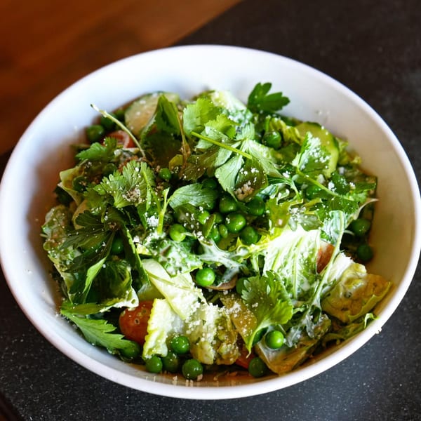A fresh Revolution House salad with greens, peas, tomatoes, and dressing in a white bowl.
