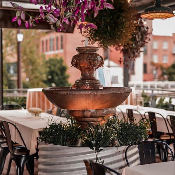 Outdoor patio at Revolution House with a decorative fountain, tables, and hanging plants.