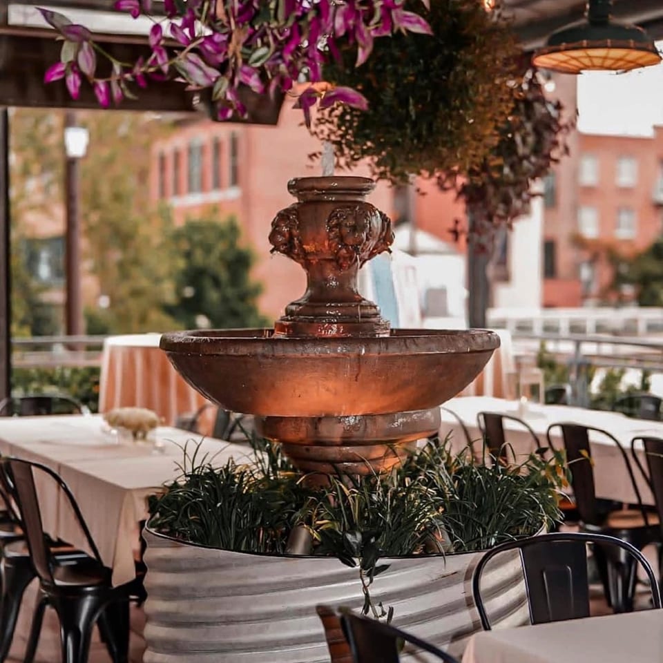 Outdoor patio at Revolution House with a decorative fountain, tables, and hanging plants.