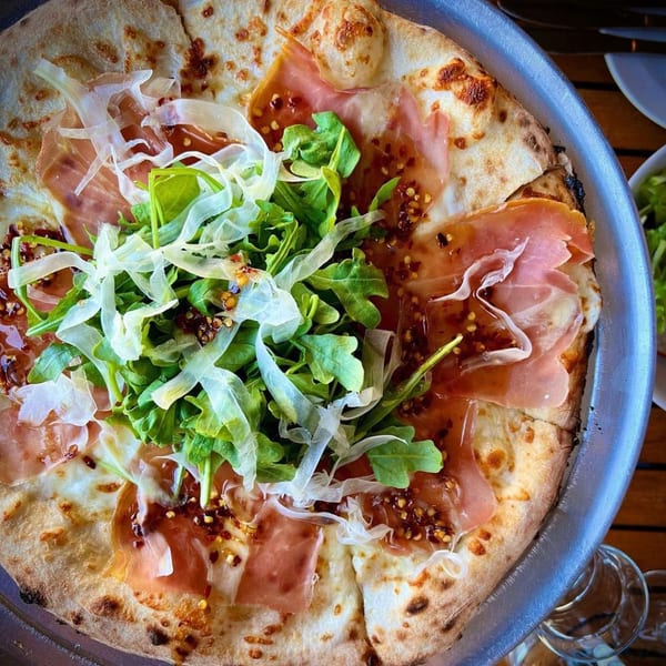 Revolution House pizza with prosciutto, arugula, shaved cheese, and a sweet chili drizzle.