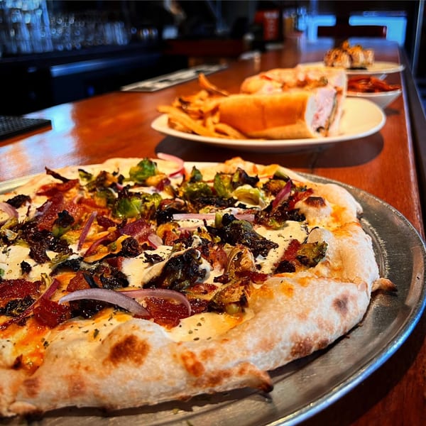 A Revolution House pizza with brussels sprouts, bacon, and red onion, with a sandwich and fries in the background.