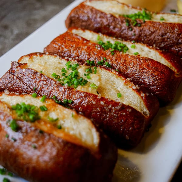 Sliced Revolution House pretzels, salted and garnished with chives, on a white rectangular plate.