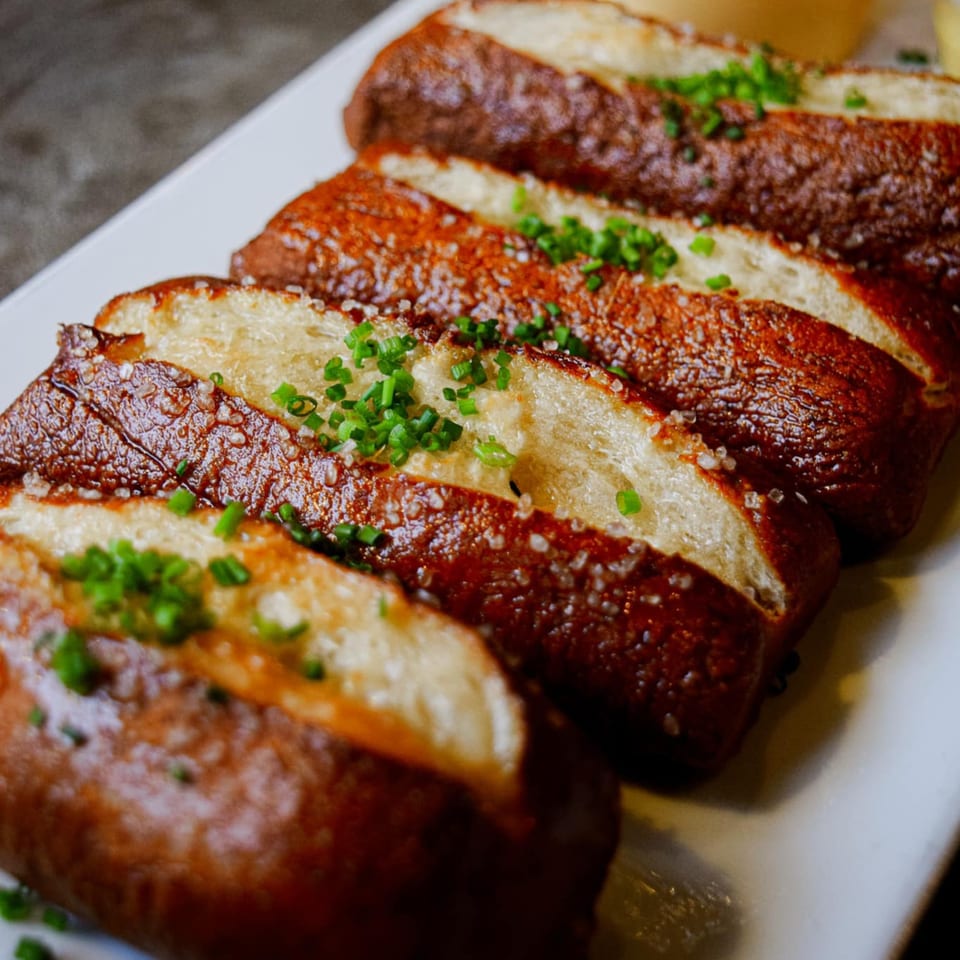 Sliced Revolution House pretzels, salted and garnished with chives, on a white rectangular plate.