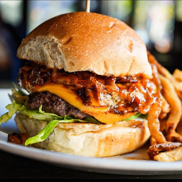 A Revolution House burger with melted cheese, caramelized onions, lettuce, and a side of fries.