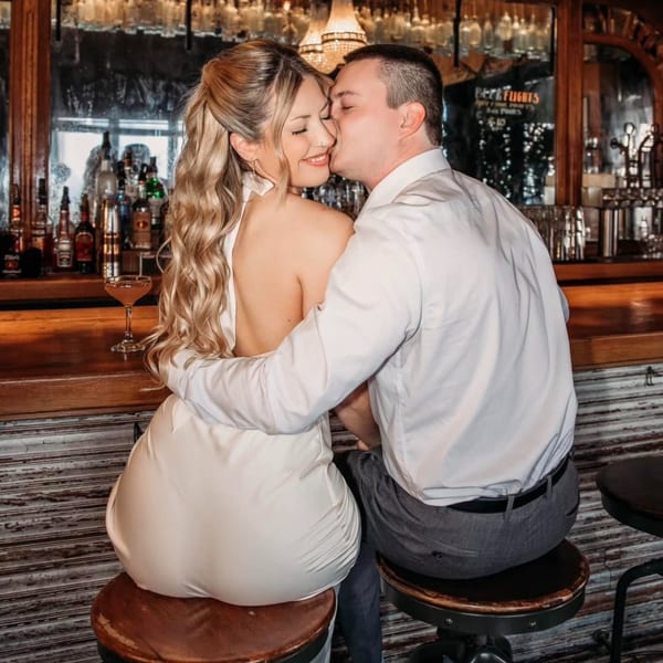A couple embracing and kissing at the bar of Revolution House, with a cocktail on the counter.