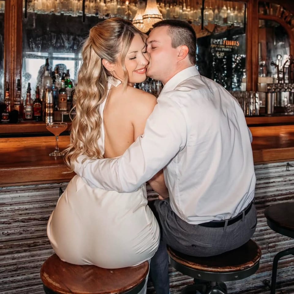 A couple embracing and kissing at the bar of Revolution House, with a cocktail on the counter.